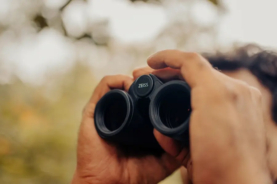 A man peering into his binoculors waiting to catch a glimpse of a flock of birds.